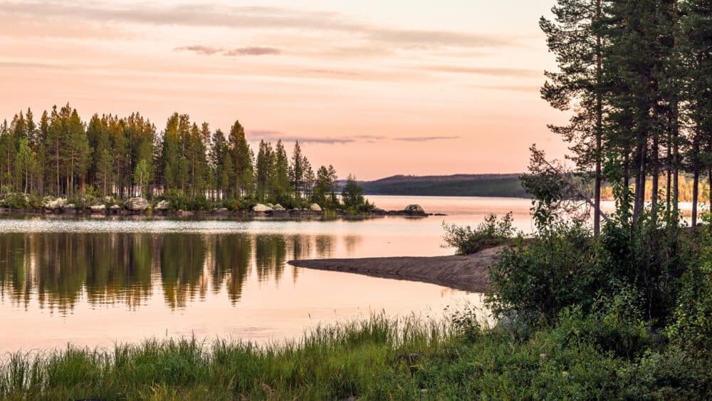 Lugn sjö i norra Sverige vid solnedgång med spegelblankt vatten, tallskog och liten ö i bakgrunden